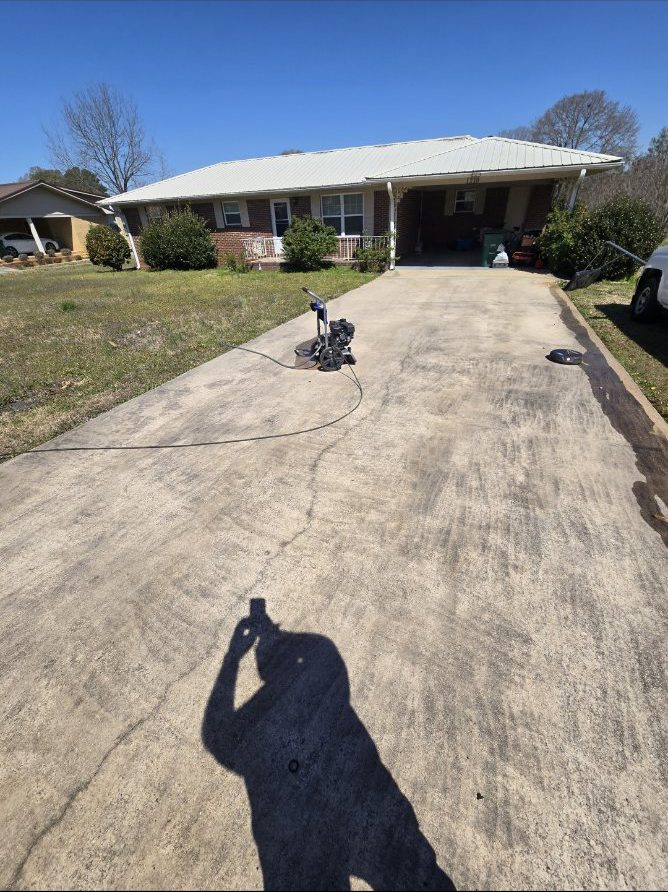 Pressure washing equipment set up on a stained driveway, cleaning under way